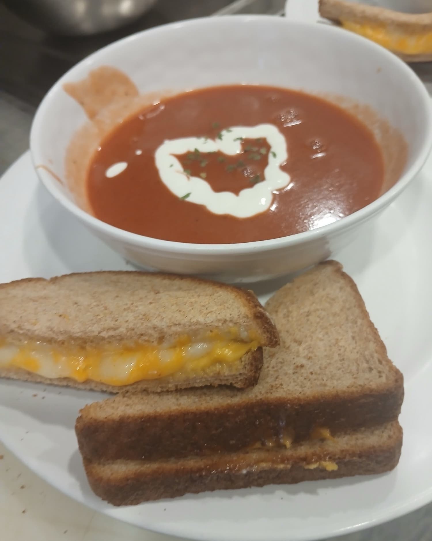 Grilled cheese on wheat bread, cut in half, beside a bowl of tomato soup with a swirl of cream